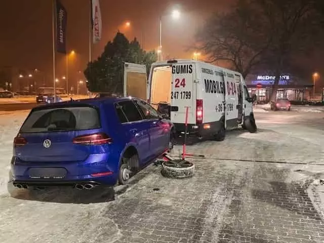 Éjszakai kerékcsere novemberben, parkolóban Téli kerékcsere parkolóban éjszaka kék Volkswagen autónál